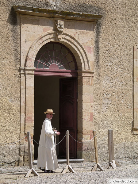 photo de moine en chapeau de paille devant entrée du cloître