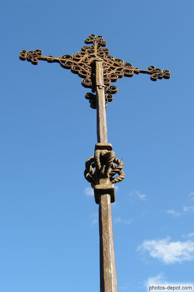 photo de croix de fer forgée au centre du cloître : la croix du grain à boule de fer emprisonnée de sa base, chef d'oeuvre de l'art de la forge
