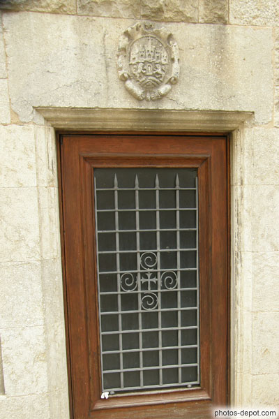 photo de porte à grille de fer ouvragé et surmontée d'un blason sculpté dans la pierre