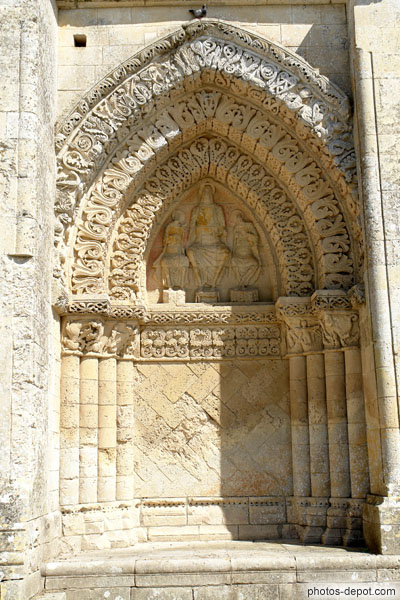 photo d'arcature du portail de droite, très mutilée, Christ entouré de St Jean et la Vierge ou St Pierre et St Paul